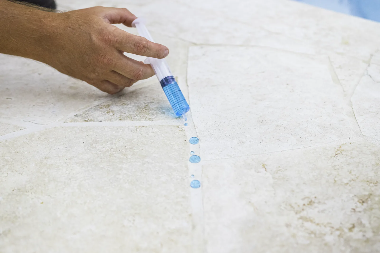 Dyed water beading along the grout of sealed travertine, showing repellency